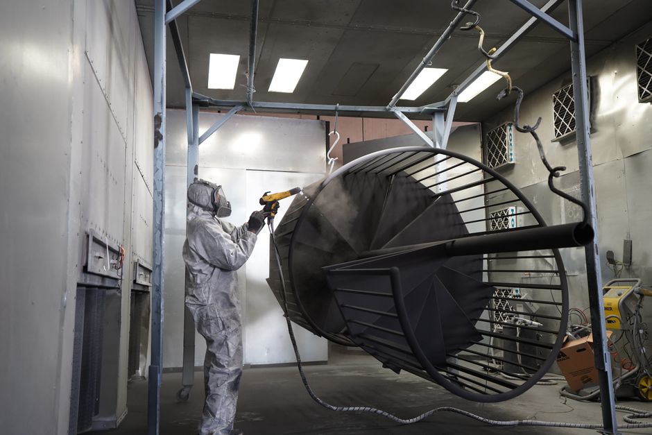 Technician performing powder coating on metal structure in industrial workshop.