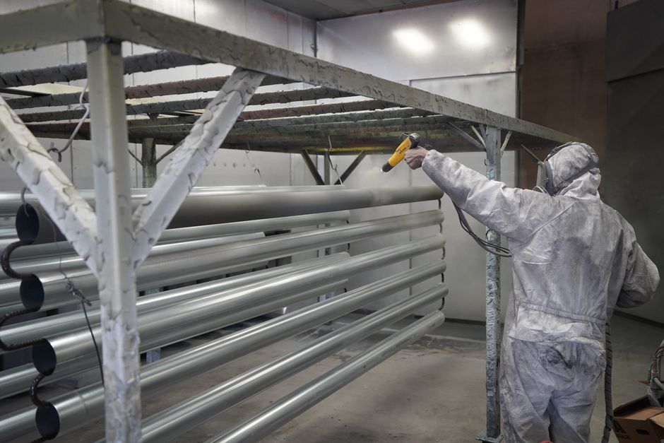 Technician applying powder coating to metal pipes in a workshop setting.